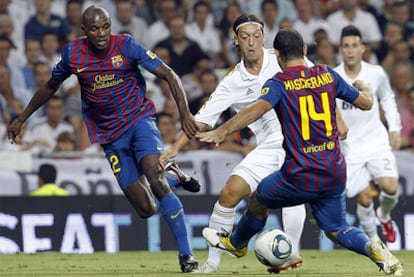 Real's Mesut Özil attempts to evade Javier Mascherano and Éric Abidal.