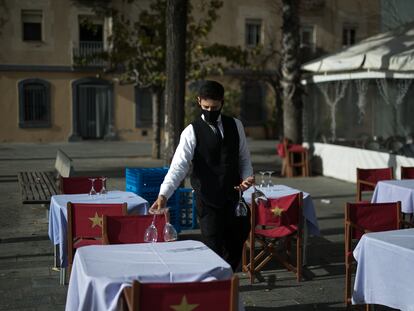 Un camarero prepara las mesas de la terraza para el turno de las comidas en Barcelona.