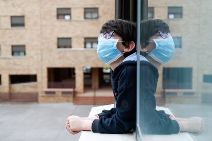 Un niño con mascarilla se asoma a la ventana de su casa durante el confinamiento.