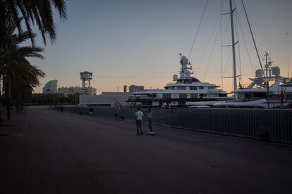 Dos jóvenes pasean al lado de varios barcos en Barcelona.
