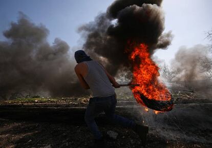 Un manifestante palestino mueve un neumático en llamas durante los enfrentamientos con las tropas israelíes tras una protesta contra el cercano asentamiento judío de Qadomem, en la aldea de Kofr Qadom en Cisjordania.