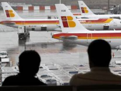 Dos pasajeros observan varios aviones de la compañia Iberia en las pistas del aeropuerto de Barajas. EFE/Archivo