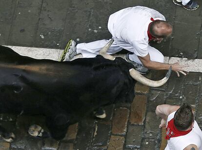 Un corredor cae ante uno de los toros de la ganadería de Victoriano del Río Cortés en el tramo de Telefónica donde se han producido las carreras con mayor riesgo al quedar rezagado el último toro, que ha estado dando vuelta sobre sí mismo y ha embestido contra el vallado, donde ha arrollado a varios mozos.