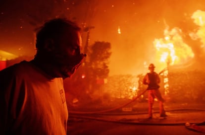 Uma pessoa passa em frente a uma casa em chamas enquanto um bombeiro tenta apagar o incêndio próximo do The Getty Center. O governador Gavin Newsom declarou estado de emergência no domingo para poder mobilizar todos os recursos disponíveis.