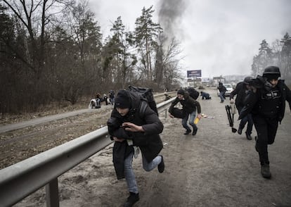 Civiles y prensa corren en las inmediaciones del río Irpin, cerca de Kiev, este domingo. Varios proyectiles de mortero han caído a lo largo de la mañana en la carretera, por la que la gente está siendo evacuada a pie en dirección a la capital.