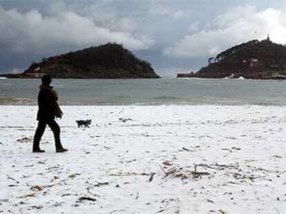 Una mujer camina con su perro sobre la nieve que cubría ayer la playa de Ondarreta, de San Sebastián.