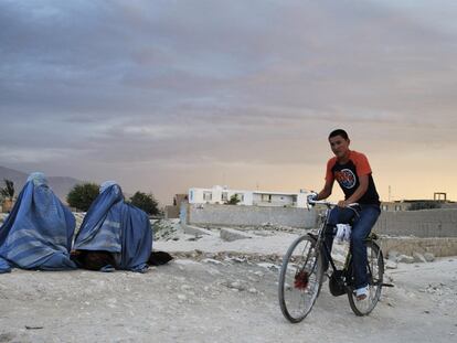 Un joven pasa en bicicleta junto a dos mujeres ataviadas con burka en el norte de Kabul.
