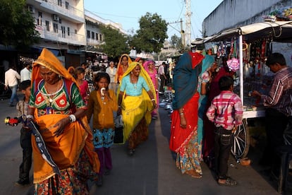 As mulheres caminham entre baias, cheias de pulseiras, roupas e tecidos