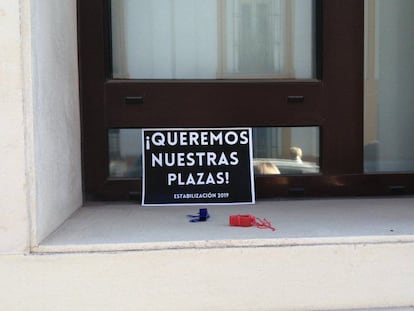 Uno de los carteles de reivindicación de los 'opositores fantasma' de Andalucía, para reclamar a la Junta que publique sus destinos definitivos, junto a varios silbatos, colocados en una ventana tras una manifestación en Sevilla.  / M. G.