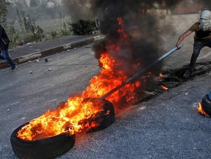 Un manifestante palestino usa un palo para mover unas ruedas ardiendo durante los enfrentamientos con las fuerzas de seguridad israelíes cerca del puesto de control de Qalandia, en Cisjordania.