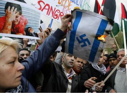 Varios manifestantes queman una bandera israelí a la que le han cambiado la estrella de David de su centro por una cruz gamada, símbolo nazi