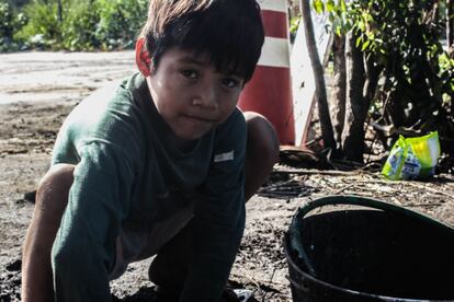 Un niño recogiendo barro en un cubo.