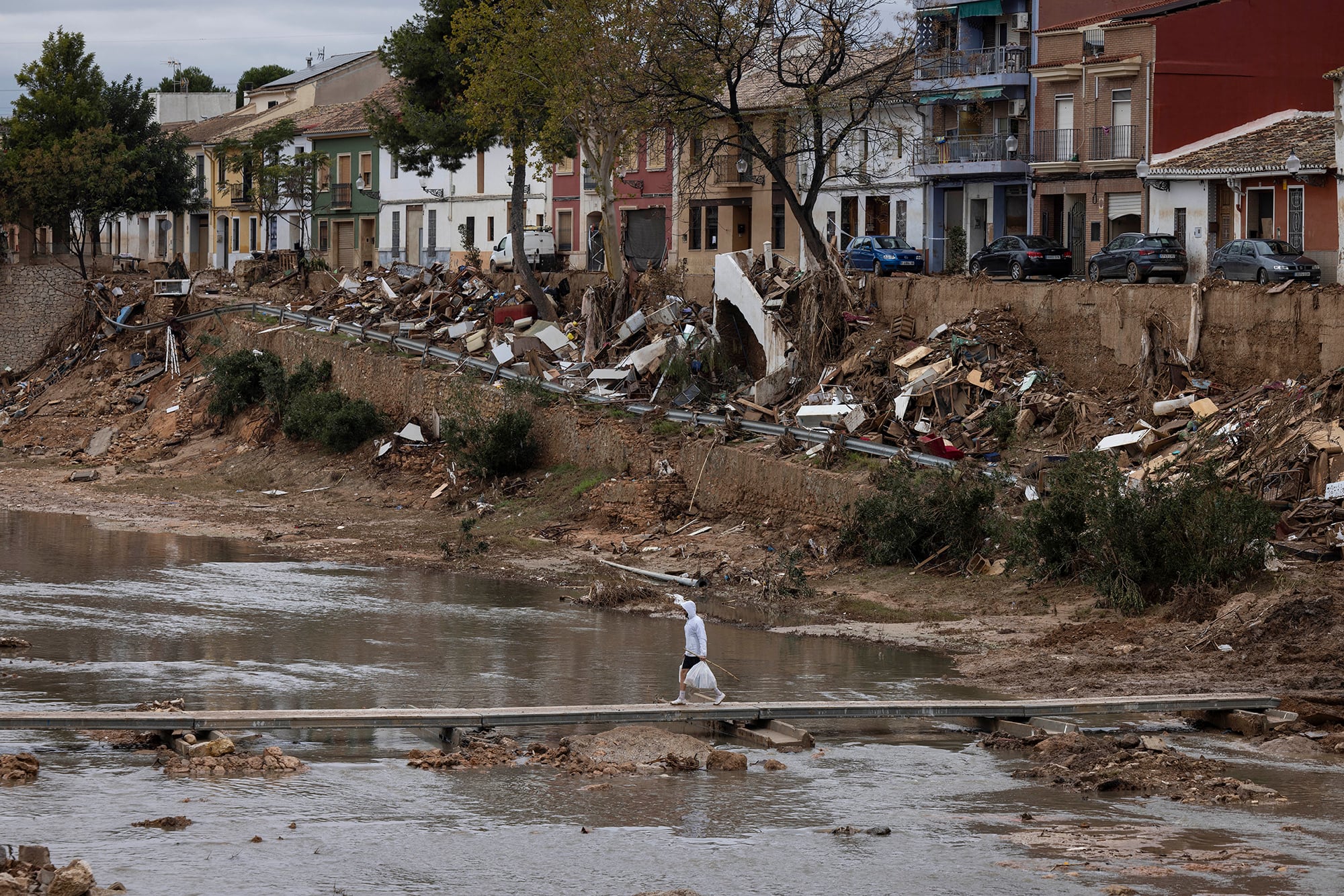 Un vecino cruza la Rambla del Poyo con un puente peatonal en Picanya (Valencia), con los márgenes del barranco llenos de escombros y destrozos, en una imagen del 13 de noviembre de 2024.