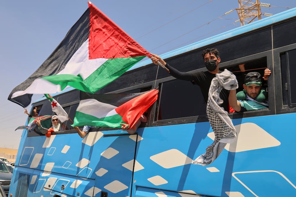 Members of a humanitarian convoy of at least 1,500 people, including activists and supporters from Algeria and Tunisia, wave Palestinian flags from a bus as the group travels toward Gaza via Egypt's Rafah Crossing, in Zawiya, Libya, Tuesday, June 10, 2025.