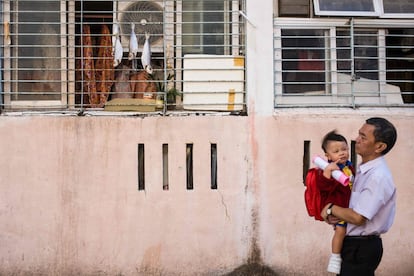Un hombre camina sosteniendo a su hijo mientras pasa junto a una residencia en cuya ventana se seca pescado, en Hong Kong.