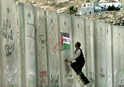 Un palestino pinta una bandera de su país con <i>paz</i> en inglés en la valla de separación que construye Israel.