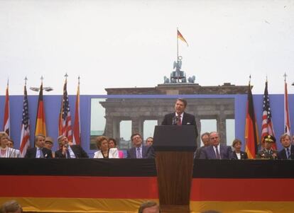 El muro de Berlín partió en dos la ciudad alemana entre 1961 y 1989. Estas palabras del entonces presidente de Estados Unidos, pronunciadas en un discurso en la Puerta de Brandenburgo de Berlín el 12 de junio de 1987 (sin líder soviético presente), no tuvieron el poder de derribar el muro, pero amplificaron la idea de que aquella pared ominosa no solo era una vergüenza para Alemania sino que atañía a “la libertad del ser humano”, como dijo Reagan. Finalmente fue el levantamiento contra la opresión soviética iniciado en Hungría y Polonia, seguido de la fuga en oleadas de refugiados de Alemania Oriental, lo que obligó al nuevo gobierno de la RDA a abrir las puertas y, en noviembre de 1989, a tirar abajo el muro. En la imagen, Ronald Reagan de pie en el podio con el canciller de Alemania occidental Helmut Kohl (derecha) y el embajador estadounidense Richard Burt (izquierda) en la Puerta de Brandenburgo, en 1987.