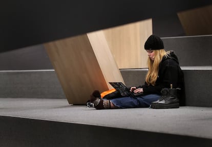 Una estudiante trabaja con su ordenador en una escalinata cubierta con moqueta en la primera planta.