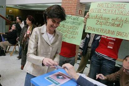 María San Gil, líder del PP vasco, vota el 17 de abril mientras seguidores de EHAK muestran carteles.