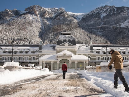 Varias personas pasan delante del edificio de la antigua estación de tren de Canfranc, hoy hotel de cinco estrellas de la cadena Barceló, cubierta por la nieve acumulada.