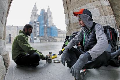 Dos peregrinos checos que llegaron desde Bordeaux (Francia), se cobijan del frío con un hornillo debajo de los arcos del palacio de Raxoi, esta mañana en la plaza de Obradoiro.