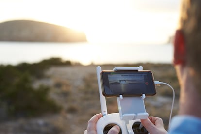 Primer plano de un hombre volando un dron sobre un paisaje costero.