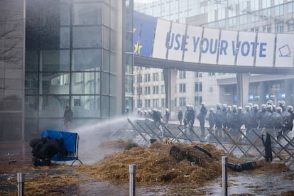 Dos manifestantes se protegen con una valla de un chorro de agua lanzado por la policía antidisturbios, este jueves en el exterior de la Eurocámara.