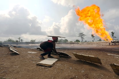 A woman sets out trays of cassava to dry near a flaring oil well in Ughelli, Nigeria.