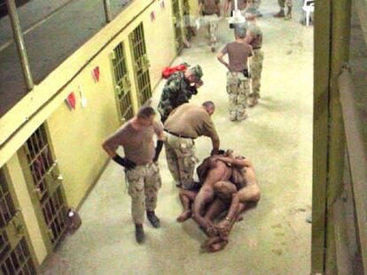 Militares estadounidenses ante presos iraquíes, desnudos y esposados unos a otros, en Abu Ghraib.