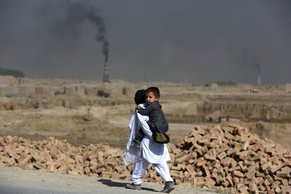 Un niño afgano camina con su hermano a cuestas frente a una fábrica de ladrillos a las afueras de Kabul (Afganistán).