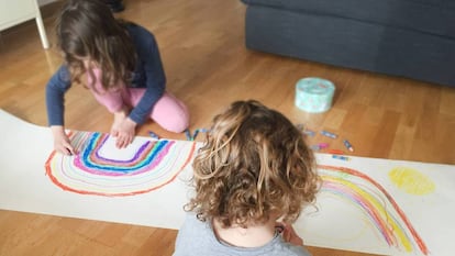 Dos niños dibujan en casa arcoíris solidarios.