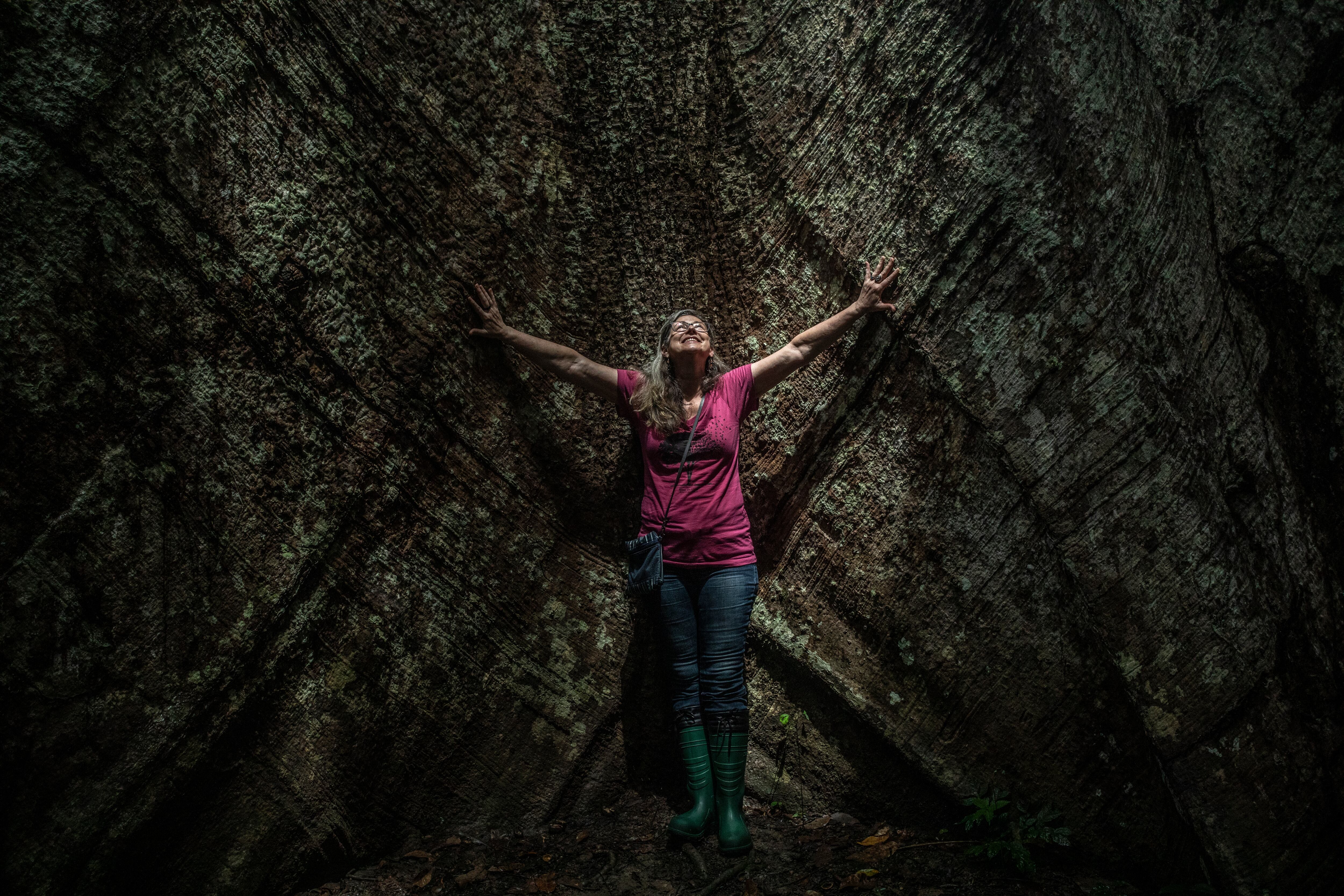 La climatóloga brasileña Luciana Gatti sonríe junto a un árbol de samaúma gigante, en el bosque nacional de Tapajós.