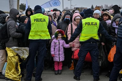 Dos agentes de policía polacos contienen este lunes a refugiados ucranios mientras esperan a ser trasladados a una estación de tren en el cruce fronterizo de Medyka en Polonia.