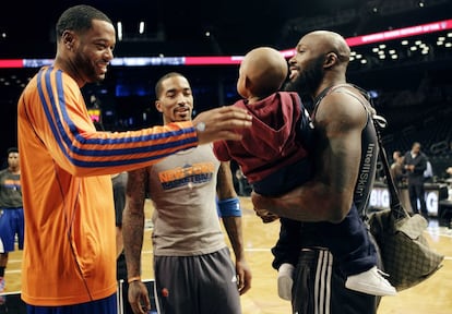 Marcus Camby y J.R. Smith, de los Knicks, charlan antes del partido con el alero de los Nets, Reggie Evans, que lleva en brazos a su hijo.