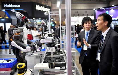 Dois participantes observam um robô industrial em uma feira de robótica em Tóquio.