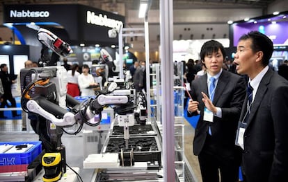 Un par de asistentes observan un robot industrial en una feria de rob&oacute;tica en Tokio. 