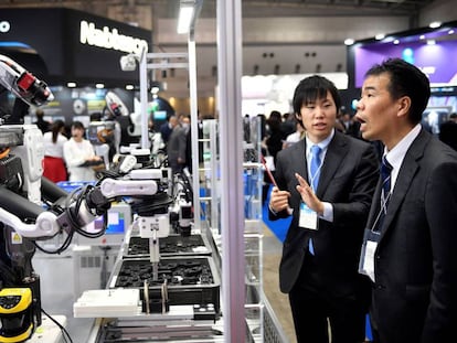 Dois participantes observam um robô industrial em uma feira de robótica em Tóquio.