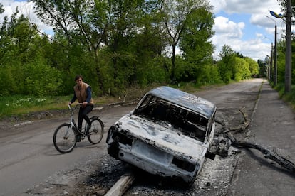 Un hombre en bicicleta pasa junto a un coche destruido por un bombardeo en una calle a las afueras de Niu-York, en Donetsk, este lunes.