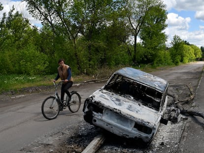 Un hombre en bicicleta pasa junto a un coche destruido por un bombardeo en una calle a las afueras de Niu-York, en Donetsk, este lunes.