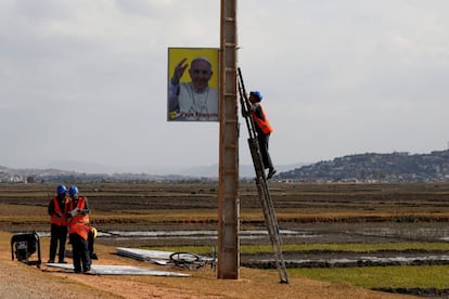 Trabajadores municipales colocan una pancarta que anuncia la visita del Papa en el poste de una carretera en Antananarivo (Madagascar).