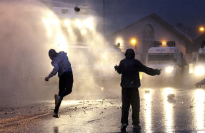 Jóvenes nacionalistas arrojan piedras contra la policía bajo el chorro de los cañones de agua anoche al norte de Belfast.