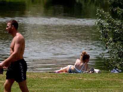 Una chica toma el sol y un chico pasea sin camiseta junto al río durante el primer día de ola de calor del 22 de mayo en Sevilla.