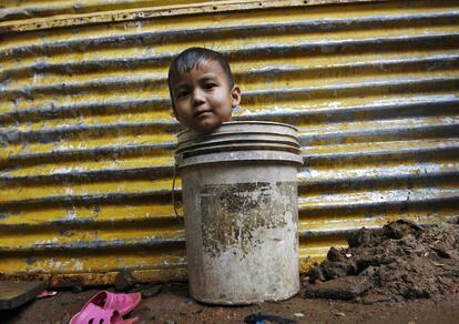 Un niño juega sentado en un un cubo mientras espera a su madre para ir a buscar agua para bañarlo, en una choza en la sureña ciudad india de Chennai.