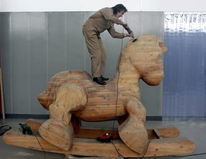 EL asturiano Adolfo Manzano repara su obra "A los héroes que fuimos", un caballo monumental de madera sobre un balancín, que se exhibirá a la entrada del centro de Arte Laboral de Gijón.