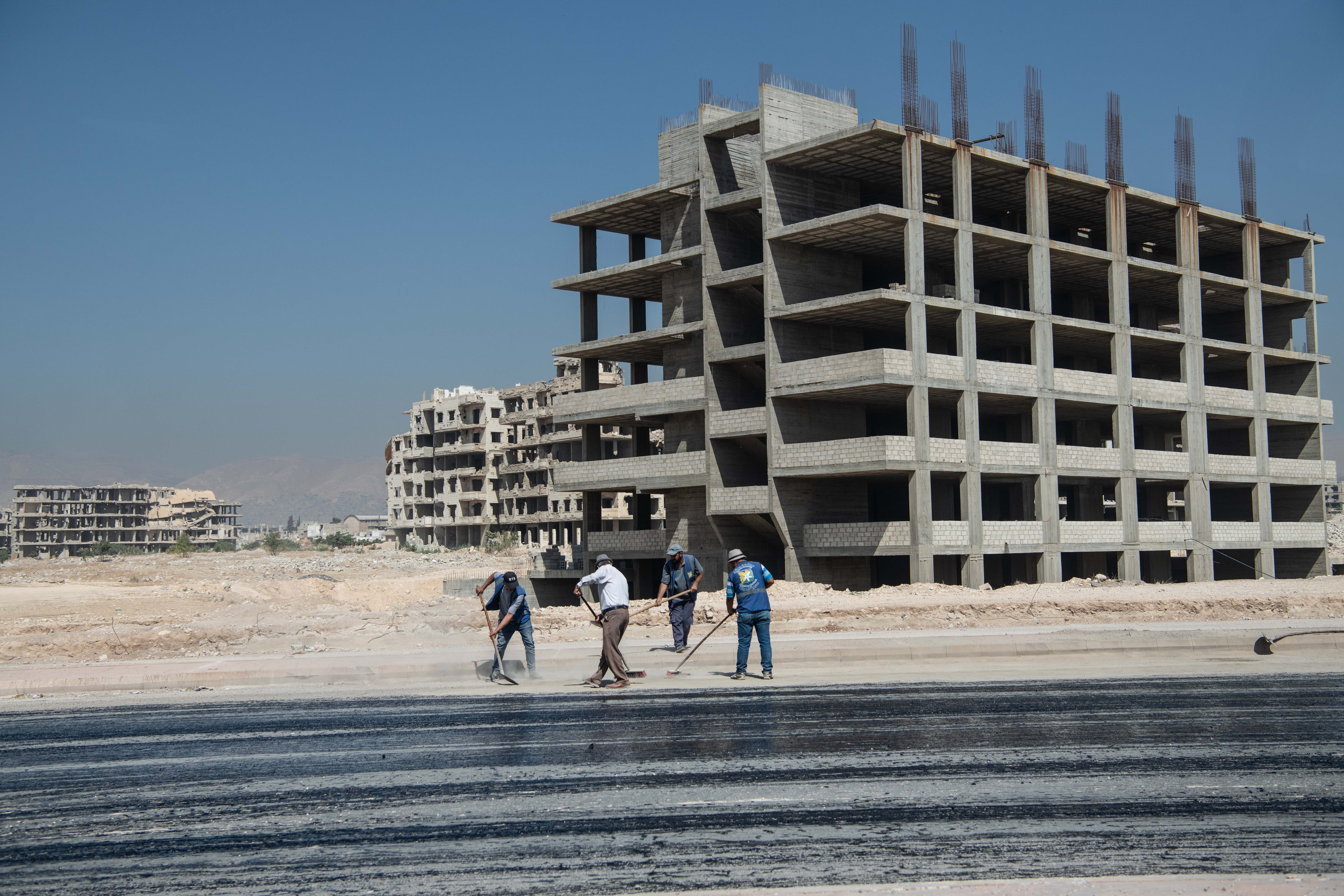 Varios trabajadores asfaltan la autopista que conecta Damasco con Homs dejando a sus espaldas construciones inacabdas de la era de Bachar el Asad, el pasado 26 de julio.