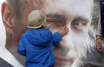 Un niño toca un cartel con la imagen del presidente ruso, Vladimir Putin.