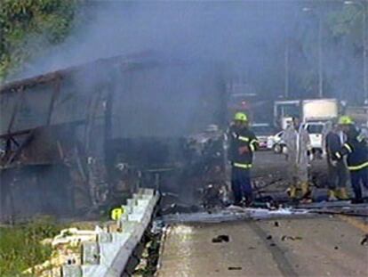 Bomberos y policía junto al autobús, calcinado por la llamas, en una imagen de la televisión.