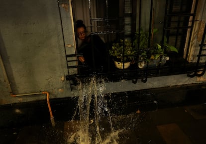 Una mujer retira agua que inundó su apartamento a través de una ventana.