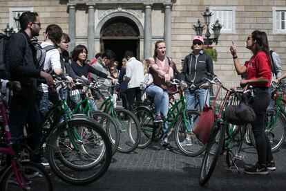 Un grup de turistes de ruta amb bicicleta escolten les explicacions de la guia turística davant del Palau de la Generalitat.