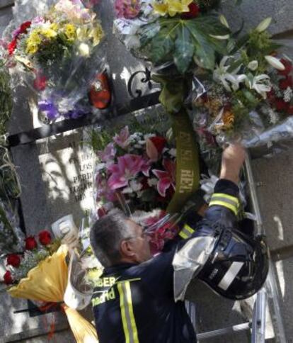 Un bomberos coloca un ramo de flores junto a la placa. 